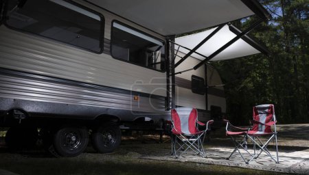 Photo for Red chairs under the awnings of an RV in a campsite surrounded by trees - Royalty Free Image
