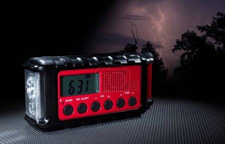 Lightning strike mingling in the trees behind a weather radio with alerts, flashlight and clock.