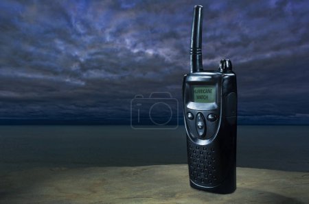Hurricane Watch warning showing on the screen of a walkie talkie with the ocean and gathering clouds behind.