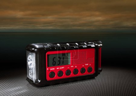 Weather radio with flashlight and clock with threatening skies in the background building over the ocean.