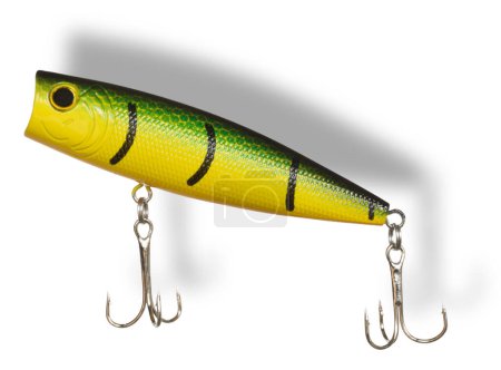 Drop shadow behind a green and yellow fishing bait used for retrieving on the surface with two treble hooks. 
