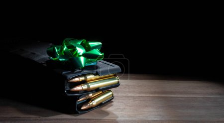 Green bow on top of two loaded high capacity AR-15 magazines on a table as a gift for a gun owner.