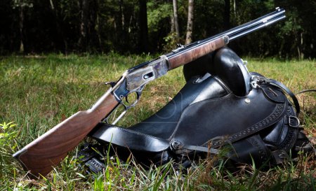 Cowboy style lever action rifle resting on a saddle in a green forest.