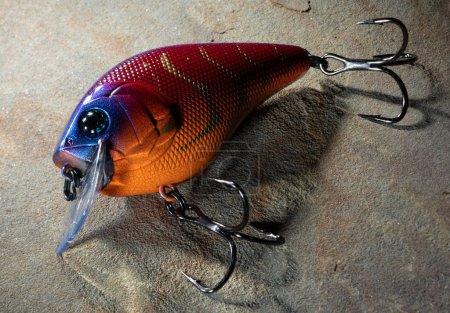 Dark fishing lure thas tis orange in color on a rock
