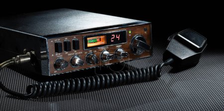 Micrófono y radio CB bidireccional en el canal 24 que puede operar en frecuencias de banda lateral que está en una alfombra de trabajo de goma con un fondo oscuro. 