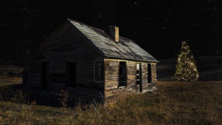 Téléchargez les photos : Cabane en bois en décomposition des colons à l'ouest avec un sapin de Noël éclairé la nuit avec un ciel clair au-dessus scintillant d'étoiles. - en image libre de droit