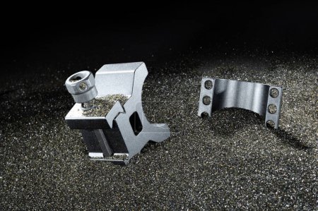 Base et anneau pour le montage d'une optique sur un pistolet entouré de sable noir et restes de copeaux de métal.