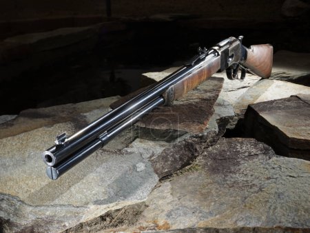 Hebel-Aktionsgewehr mit Holzstock sitzt auf Steinen mit dunklem Hintergrund.