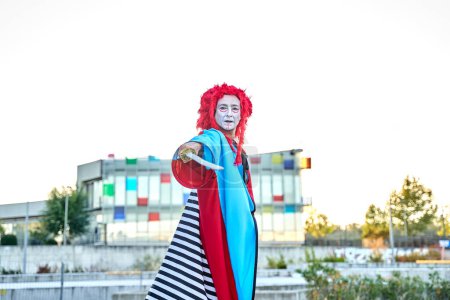 Photo for Stilt walker in colorful costume holding a sword looking at the camera in the open air with a colorful building in the background. - Royalty Free Image