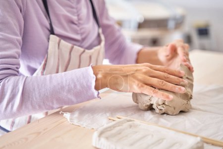Foto de Mujer alfarero trabaja con arcilla, cerca de vista superior manos femeninas sostienen un pedazo de arcilla húmeda en sus manos. El alfarero crea un producto. Foto de alta calidad - Imagen libre de derechos