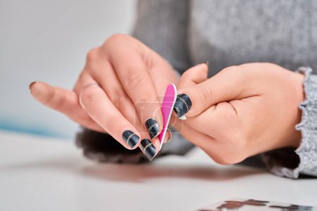 Photo for Woman filing and shaping her nails with adhesive nail decals. Manicure and beauty concept. - Royalty Free Image