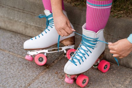 Detalle de cerca de unas manos de patinadores atando los cordones de un par de patines de cuatro ruedas. 