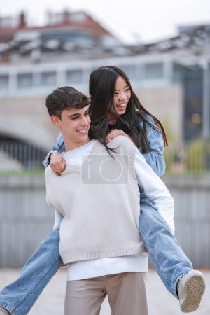 Téléchargez les photos : Jeune couple profite d'un moment amusant et affectueux, avec la fille chevauchant sur les garçons dos, par une journée nuageuse - en image libre de droit