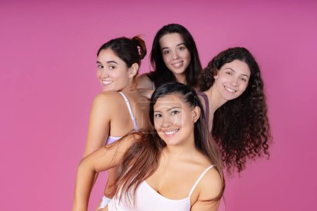 Photo for Four diverse women standing in a line, smiling over their shoulders in a body positive underwear campaign on a pink backdrop. - Royalty Free Image