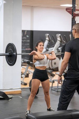Focused female athlete getting ready to perform a barbell exercise with a spotter nearby. 
