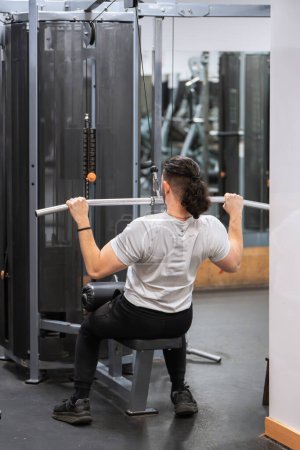 Hombre atlético realizando ejercicio de retirada de lat en una máquina en un centro de fitness. 