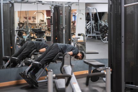 Homme concentré effectuant une extension du dos sur l'équipement de gymnastique, avec réflexion dans le miroir. 