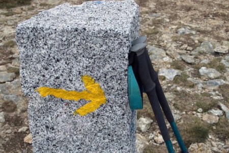 Photo for Nordic walking poles leaning against a granite pole. Granite post with arrow sign indicating the direction for hikers. Top of La Bola del Mundo in Navacerrada, Spain. - Royalty Free Image