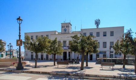 Foto de Locorotondo, Italy. 06 27 19. Facade of the town hall in Aldo Moro square. A simple square decorated with some trees, with benches to rest and lampposts for night lighting. - Imagen libre de derechos