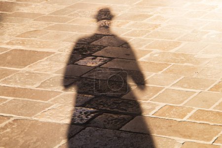Foto de Mi sombra en el soleado terreno de Lecce, Italia. Larga sombra de un hombre con sombrero, al atardecer sobre un suelo de adoquín beige. - Imagen libre de derechos