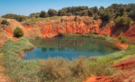 Artificial lake created by flooding an old bauxite quarry in Otranto, Italy. Lagoon surrounded by reeds and with a strong color contrast between the reddish earth and the emerald water.