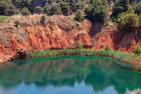 Téléchargez les photos : Lac artificiel créé par l'inondation d'une ancienne carrière de bauxite à Otrante, en Italie. Lagune entourée de roseaux et avec un fort contraste de couleur entre la terre rougeâtre et l'eau émeraude. - en image libre de droit