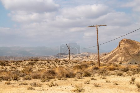 Old electrical conduction poles, now in disuse. Desert landscape in the vicinity of Tabernas, Almeria, Spain. Arid landscape made up of hills and ravines with little vegetation.
