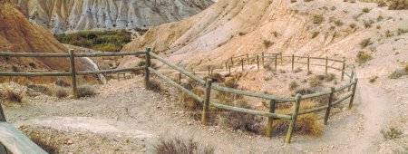 Foto de Pasarelas de madera y escaleras de un sendero en terreno árido para descender a un barranco. Paisaje árido de la Rambla de Genaro en el desierto de Tabernas, Almería, España. - Imagen libre de derechos