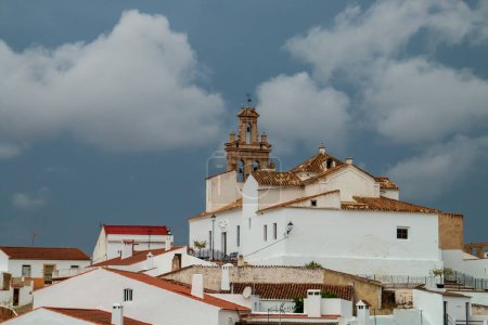 Iglesia Católica de Nuestra Señora de las Flores en Sanlúcar de Guadiana, Huelva, España. Iglesia situada en la cima de una colina rodeada de casas encaladas en un día tormentoso.