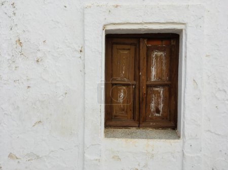 Rustic wooden window in a whitewashed stone wall in Sanlucar de Guadiana, Spain. Closed and painted brown window of an old and uninhabited house.