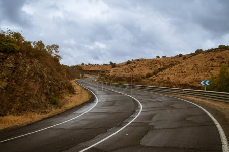 Camino pavimentado con curvas y mojado por la reciente lluvia otoñal. Carretera rural HU-4401 en el km 14 en un día lluvioso en Sanlúcar de Guadiana, Andalucía, España.