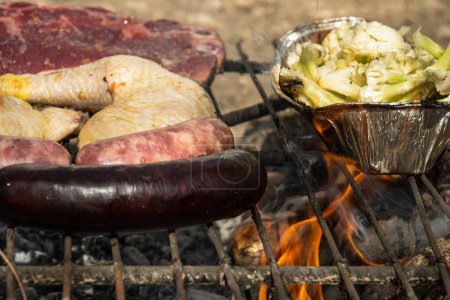 Photo for Sausages, steaks, chicken thighs and cauliflower grilling outdoors - Royalty Free Image
