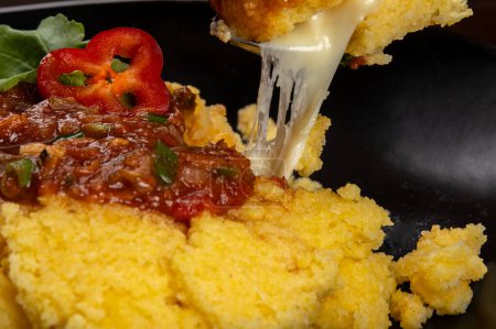 Foto de Plato negro de polenta con salsa de tomate y harina de queso derretido - Imagen libre de derechos