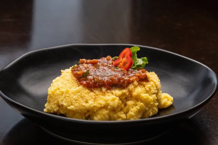 Photo for Black plate of polenta with tomato sauce and melted cheese flour - Royalty Free Image