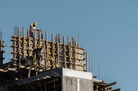 Téléchargez les photos : Bâtir au-dessus du ciel : les travailleurs méconnaissables construisent en toute sécurité - en image libre de droit
