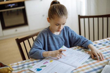 una niña independiente de 7 años de edad, haciendo su tarea escolar en casa en la cocina