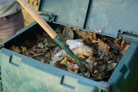 Foto de Un joven se mezcla en los residuos orgánicos arrojados al compost al aire libre bin.The compost bin se coloca en un jardín en casa para reciclar los residuos orgánicos producidos en el hogar y el jardín y producir fertilizante orgánico. Concepto de reciclaje y sostenibilidad - Imagen libre de derechos