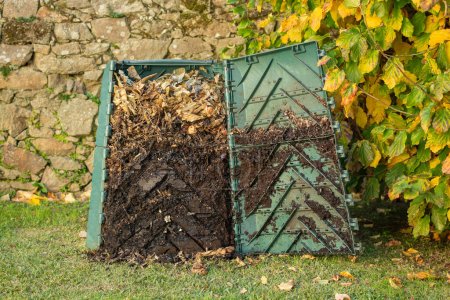 Outdoor compost bin was opened to extract mature compost formed in the down part.The compost bin is placed in a home garden to recycle organic waste produced in home and garden. Concept of recycling and sustainability