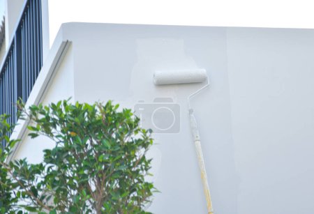 Ein Arbeiter streicht mit einer Farbrolle die Wände des Hauses mit einer Grundierung.