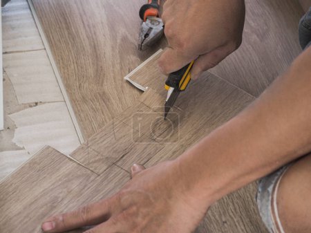Photo for A technician is cutting luxury vinyl floor tiles with a cutter to lay the floor before placing it on the leveling foam. - Royalty Free Image