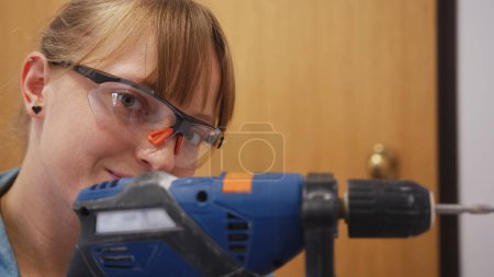 Foto de Closeuo view of a woman with safety glasses using a drill into a wall, repair concept. High quality photo - Imagen libre de derechos