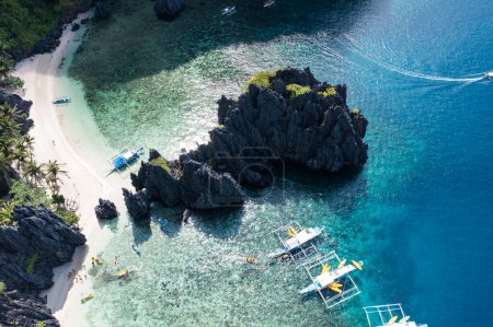 Luftaufnahme verschiedener touristischer Bangka-Boote an einem sonnigen Tag, mit seinem tropischen Strand und den wunderschönen felsigen Bergen, die Secret Lagoon, El Nido, Palawan umgeben.