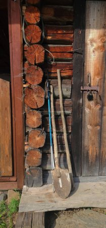 Gartengeräte und ein alter Skistock stehen vor den verschlossenen Türen eines massiven Holzschuppens.