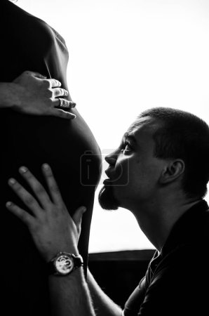 Photo for A man kisses his pregnant wife on the stomach. Black and white photo - Royalty Free Image