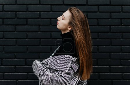 Photo for A woman in a coat stands in front of a black brick wall - Royalty Free Image