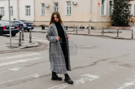 Photo for A woman crossing the street in a coat and jeans - Royalty Free Image