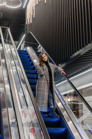 Photo for A girl in a coat goes down the escalator - Royalty Free Image