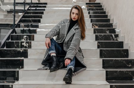 Photo for A girl in a coat sits on the stairs - Royalty Free Image