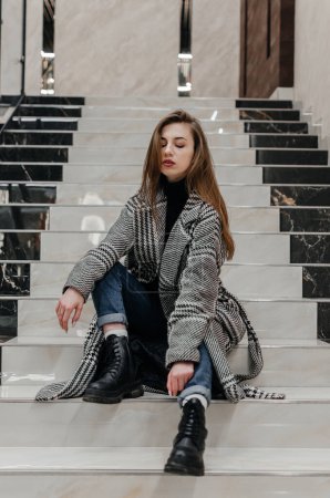 Photo for A girl in a coat sits on the stairs - Royalty Free Image