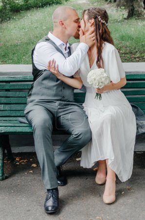 Téléchargez les photos : La mariée et le marié baisent assis sur un banc - en image libre de droit